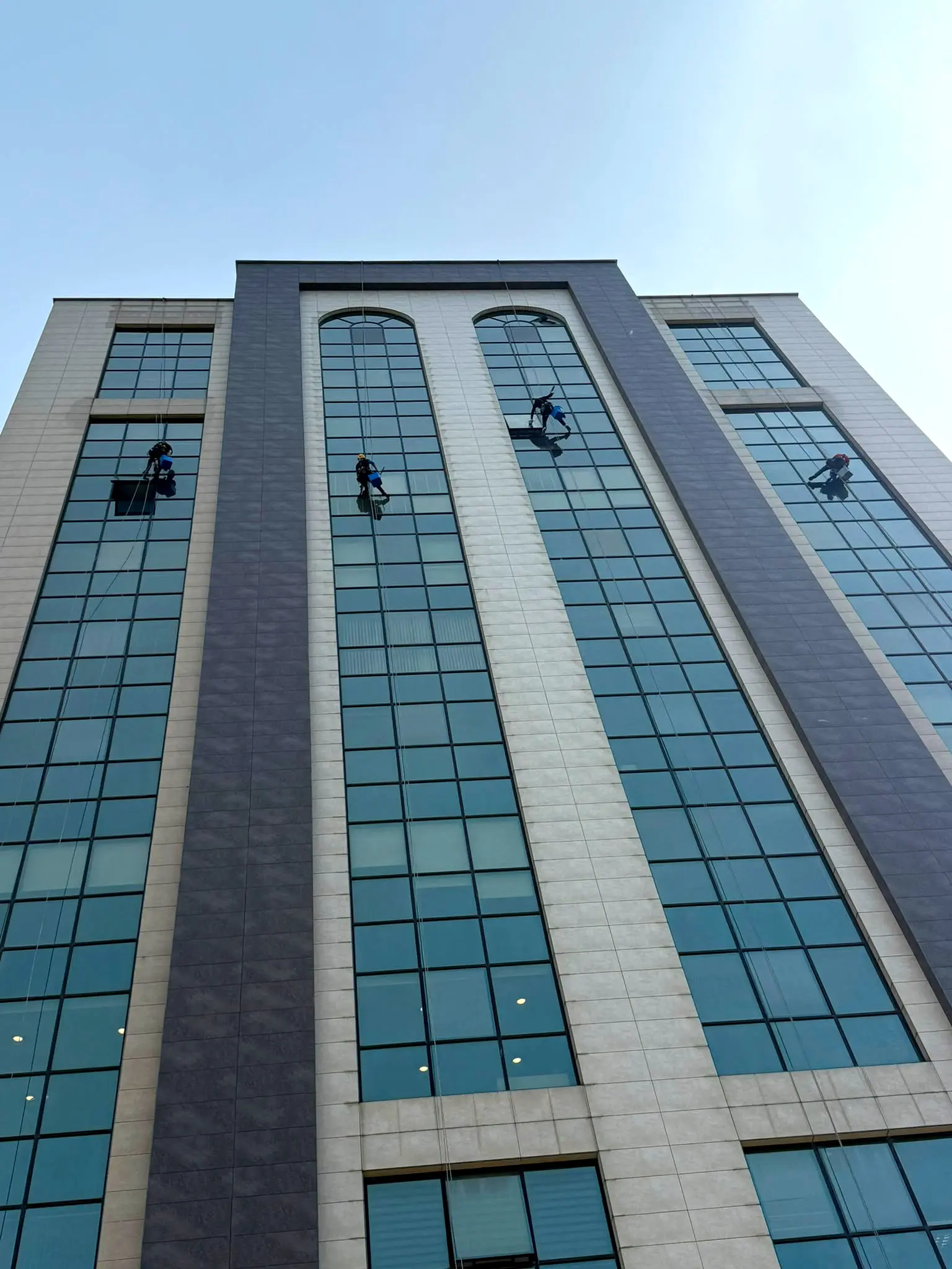 Taş ve cam cepheli plazada iple erişimle temizlik yapan 4 kişilik ekip